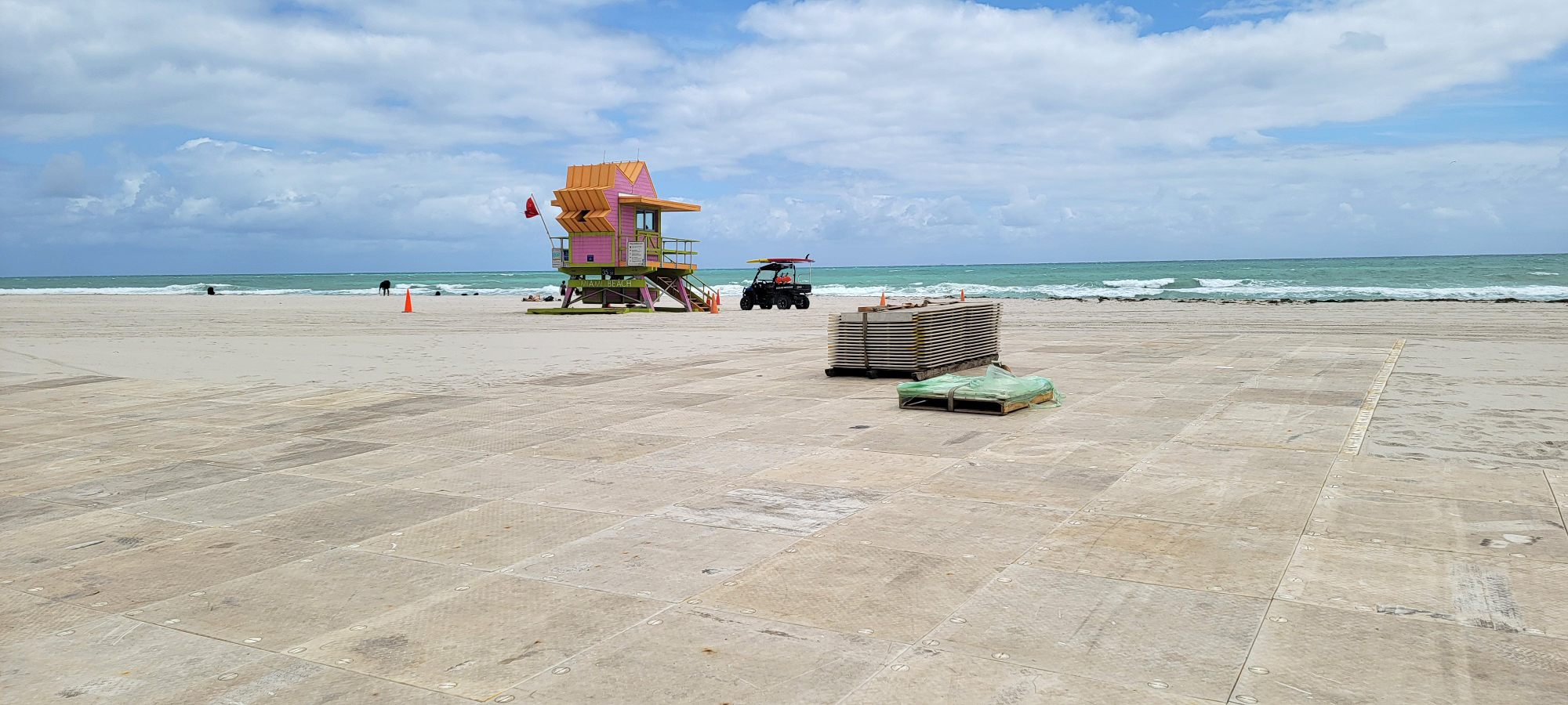 Beach with ocean in background, protective flooring, pallet of flooring panels, and structure.